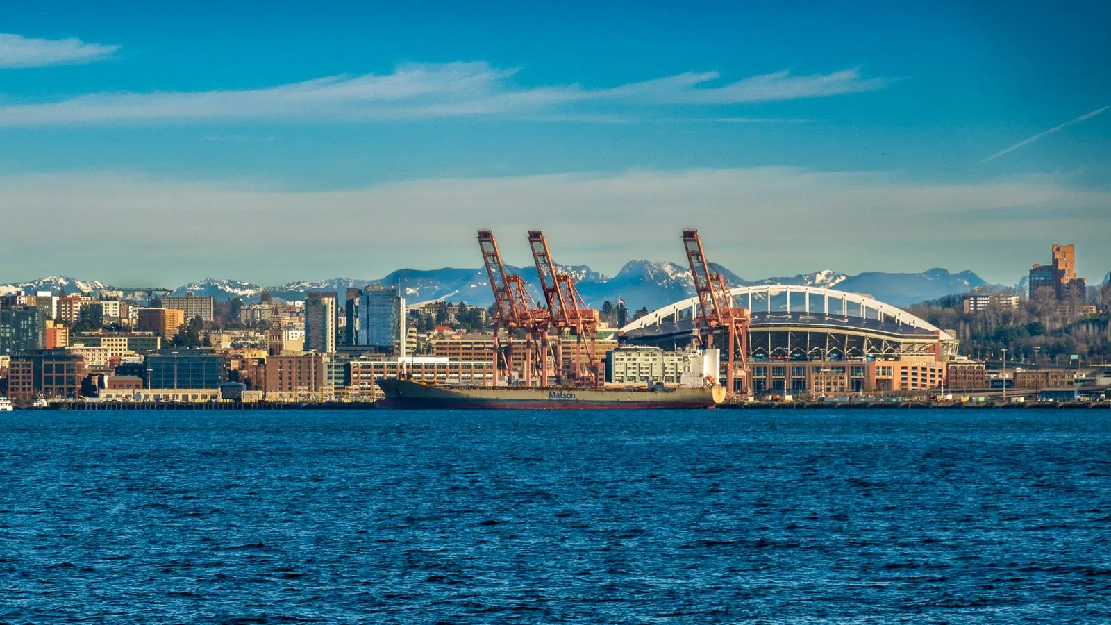 Seattle skyline featuring stadium and cranes by the waterfront on a clear day.